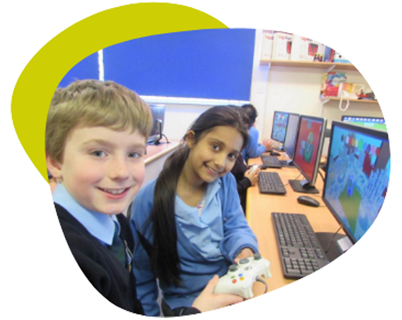 Smiling school children at the computer with games controller.
